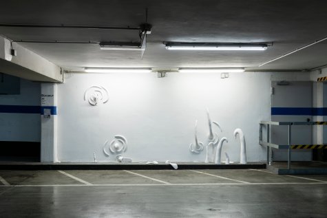Installation view of the work "tschuss" in the parking lot of the Kunsthalle. Various sculptures are mounted on the wall.