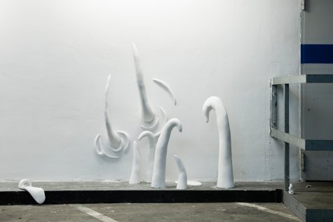Installation view of the work tschüss in the parking lot of the Kunsthalle. Various sculptures are mounted on the wall.