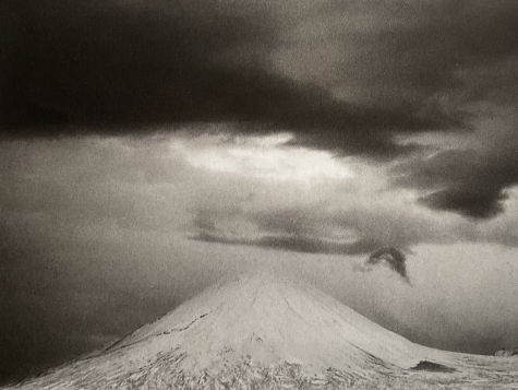 Schwarzweiß-Fotografie einer verschneiten Bergspitze vor einem verhangenen Himmel. Das Bild wirkt duster.