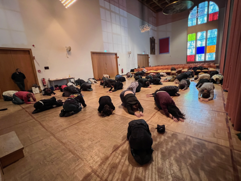 Die Fotografie zeigt die Innenansicht eines Raumes. Mehrere Personen knien nieder, ihre Oberkörper und Arme liegen auf dem Boden.