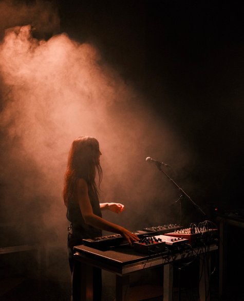 Sepiafarbene Fotografie einer Frau mit langen Haaren an einem Mischpult. Sie ist in Nebel gehüllt.
