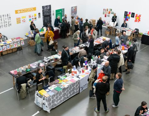 Fotografie von der Kunstbuchmesse zeigt mehrere Aussteller*innentische und Menschen von schräg oben.