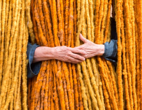 Eine Menge gelbe Schnüre hängen herab und eine Person umfasst einen Strang von ihnen. Man sieht nur ihre Hände.