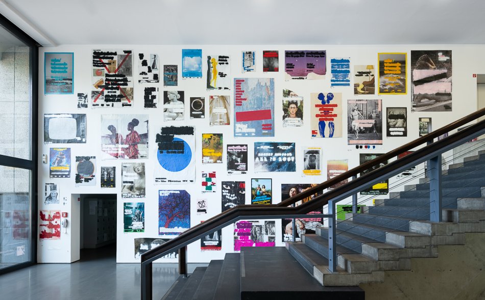 We look sideways at a staircase. On the wall in the background hang many painted posters.