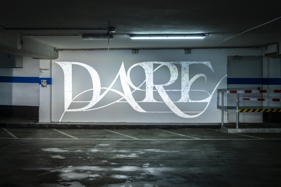 Das Wort Dare steht leuchtend auf einer weißen Wand.